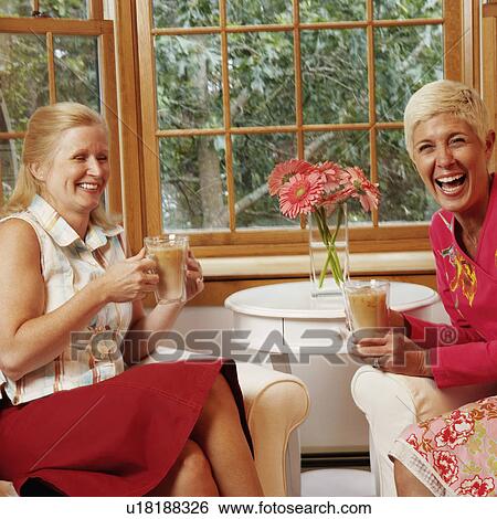Stock Photograph - Mature woman and a senior woman holding mugs of coffee and laughing. Fotosearch