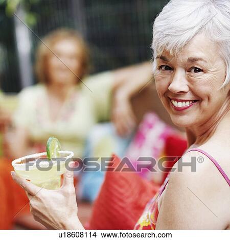 Picture - Portrait of a mature woman holding a glass of lemonade and smiling. Fotosearch