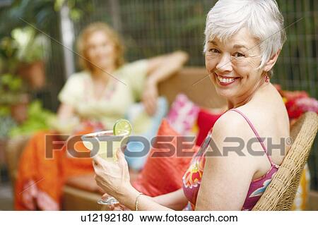 Stock Image - Portrait of a mature woman holding a glass of lemonade and smiling. Fotosearch
