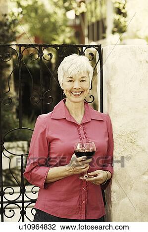 Stock Image - Portrait of a senior woman holding a glass of red wine. Fotosearch