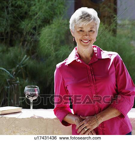 Stock Photograph - Portrait of a senior woman leaning against a wall on a terrace. Fotosearch