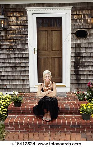 Picture - Portrait of a senior woman sitting at the front stoop of house. Fotosearch