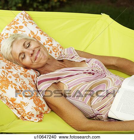 Stock Image - Side profile of a senior woman lying in a hammock with her eyes closed. Fotosearch