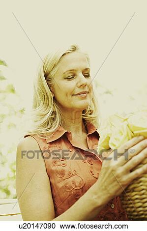 Stock Image - Close-up of a mature woman arranging flowers in a vase. Fotosearch