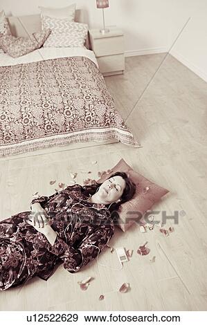Stock Photo - High angle view of a mature woman lying on a wooden floor and listening to an MP3 player. Fotosearch
