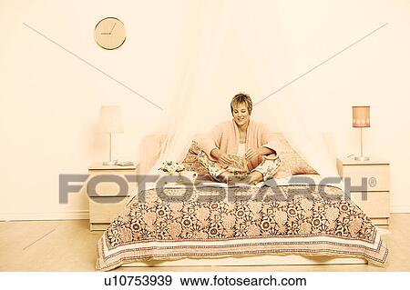 Stock Photo - Mature woman sitting on the bed and reading a book. Fotosearch