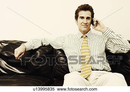 Stock Photography - Portrait of a businessman sitting on a couch and talking on a mobile phone. Fotosearch