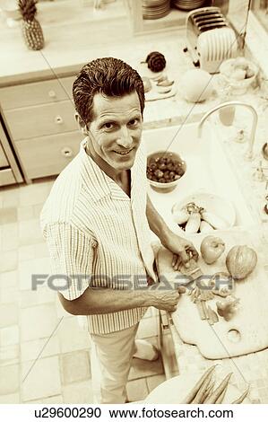 Stock Image - Portrait of a mature man cutting vegetables in a kitchen. Fotosearch