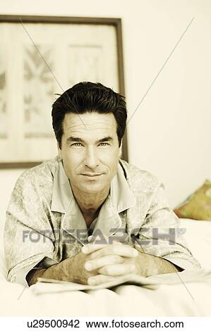 Stock Image - Portrait of a mature man lying on the bed with a newspaper. Fotosearch