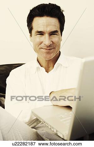 Stock Photo - Portrait of a mature man using a laptop and smiling. Fotosearch