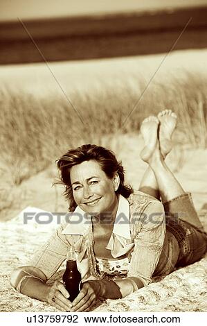 Portrait of a mature woman lying on the beach and holding a bottle View Large Photo Image Stock Image - Portrait of a mature woman lying on the beach and holding a bottle. Fotosearch