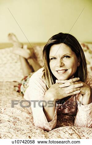 Stock Photo - Portrait of a mature woman lying on the bed and smiling. Fotosearch