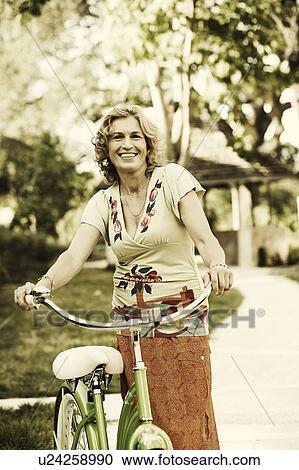 Stock Image - Portrait of a mature woman standing with a bicycle. Fotosearch