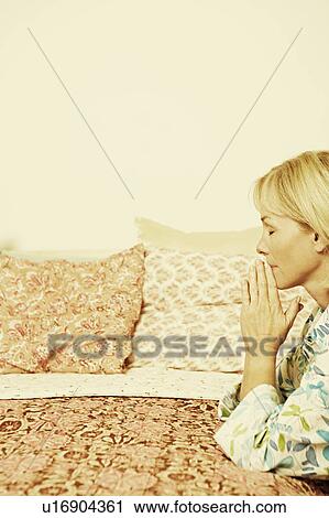 Stock Image - Side profile of a mature woman praying in a bedroom. Fotosearch