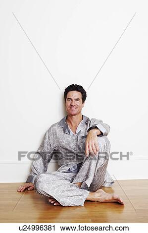 Stock Image - Portrait of a mature man sitting on the floor with his hand on his knee. Fotosearch
