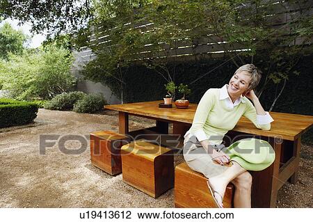 Mature woman sitting on a stool and smiling View Large Photo Image Stock Image - Mature woman sitting on a stool and smiling. Fotosearch
