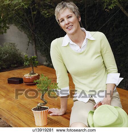 Stock Image - Portrait of a mature woman sitting on a table and smiling. Fotosearch