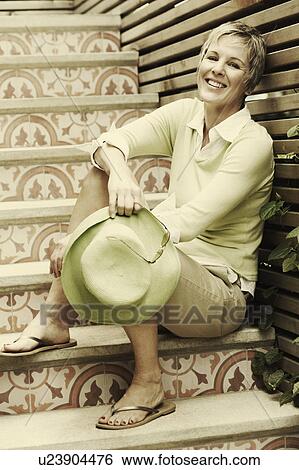 Stock Photograph - Portrait of a mature woman sitting on a staircase and smiling. Fotosearch