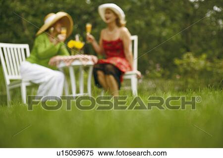 Stock Photography - Two women sitting in a garden holding glasses of juice. Fotosearch