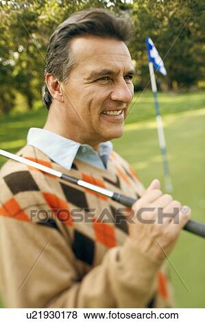 Stock Photo - Close-up of a mature man carrying a golf club and smiling at a golf course. Fotosearch