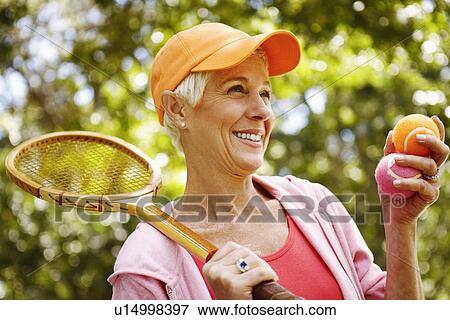 Close-up of a mature woman holding a tennis racket and two tennis balls View Large Photo Image Stock Photo - Close-up of a mature woman holding a tennis racket and two tennis balls. Fotosearch