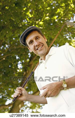 Stock Photography - Low angle view of a mature man holding a golf club and a golf ball. Fotosearch