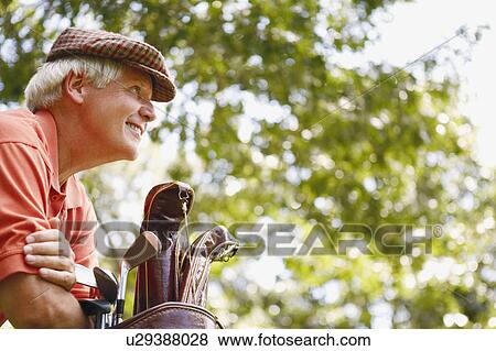 Low angle view of a mature man leaning on a golf bag and smiling View Large Photo Image Stock Photo - Low angle view of a mature man leaning on a golf bag and smiling. Fotosearch