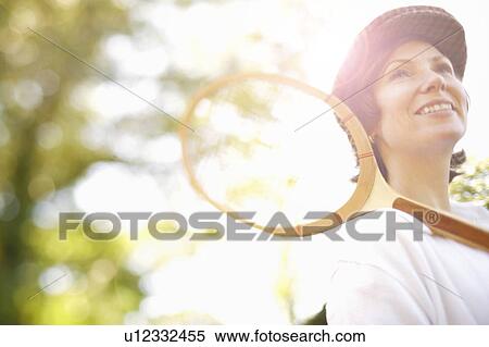 Stock Photography - Low angle view of a mid adult woman holding a tennis racket and smiling. Fotosearch
