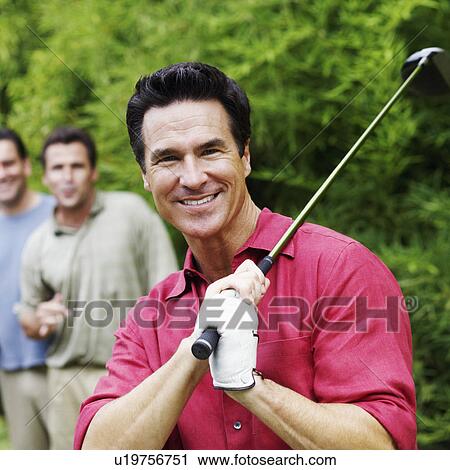 Stock Image - Mature man holding a golf club with his friends standing behind him. Fotosearch
