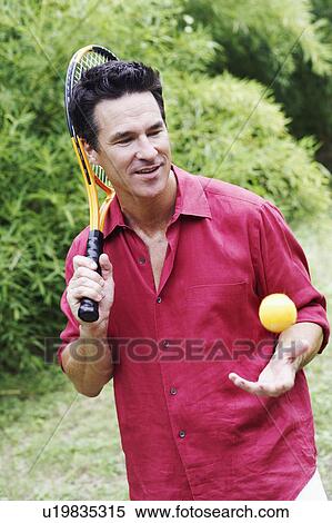 Stock Photography - Mature man holding a tennis racket and tossing a tennis ball. Fotosearch
