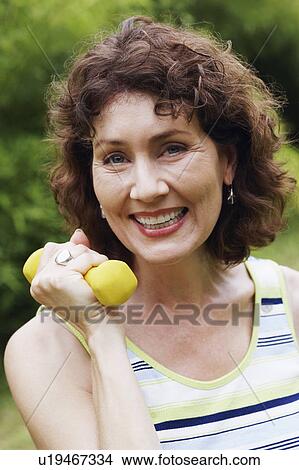 Portrait of a mature woman exercising with a dumbbell and smiling View Large Photo Image Picture - Portrait of a mature woman exercising with a dumbbell and smiling. Fotosearch
