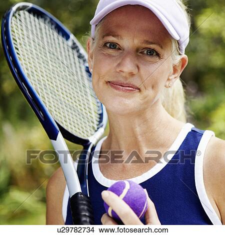 Picture - Portrait of a mature woman holding a tennis racket and a tennis ball. Fotosearch
