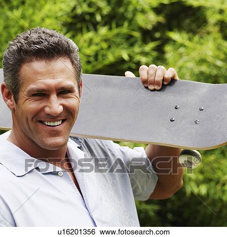 Portrait of a mid adult man carrying a skateboard on his shoulder and smiling View Large Photo Image Stock Photograph - Portrait of a mid adult man carrying a skateboard on his shoulder and smiling. Fotosearch
