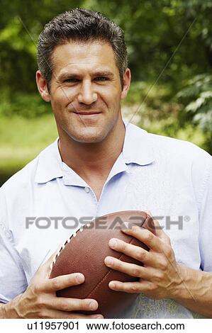 Stock Image - Portrait of a mid adult man holding a football. Fotosearch
