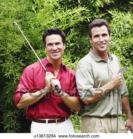 Picture - Two mature men holding golf clubs and smiling. Fotosearch