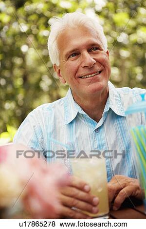 Stock Photo - Close-up of a mature man holding a glass of a juice and smiling. Fotosearch