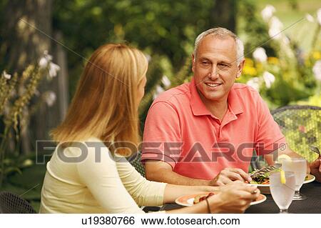 Stock Photograph - Mature man with a mid adult woman sitting at the table with plates of salad in front of them. Fotosearch