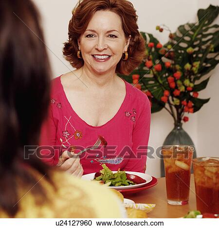 Stock Image - Mature woman sitting at a dining table with her friend and smiling. Fotosearch