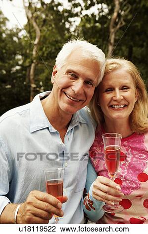 Stock Image - Portrait of a mature couple holding champagne flutes and smiling. Fotosearch