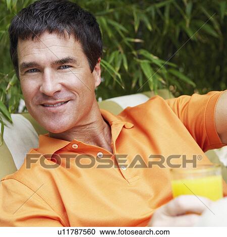 Stock Image - Portrait of a mature man holding a glass of juice. Fotosearch