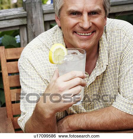 Stock Photograph - Portrait of a mature man holding a glass of lemon juice and smiling. Fotosearch