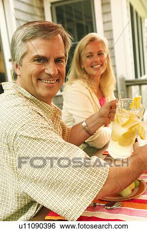 Stock Photograph - Portrait of a mature man pouring lemon juice in a glass with a mature woman sitting beside her. Fotosearch