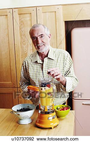 Stock Image - Portrait of a mature man preparing mango shake. Fotosearch