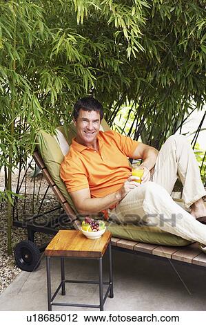Stock Image - Portrait of a mature man reclining on a lounge chair and holding a glass of juice. Fotosearch