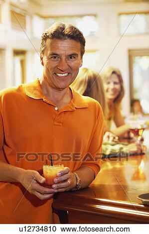 Stock Image - Portrait of a mature man standing at a bar counter and smiling. Fotosearch