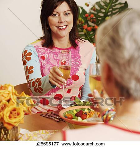 Stock Photo - Portrait of a mature woman and her friend toasting with a champagne flute at a dining table. Fotosearch