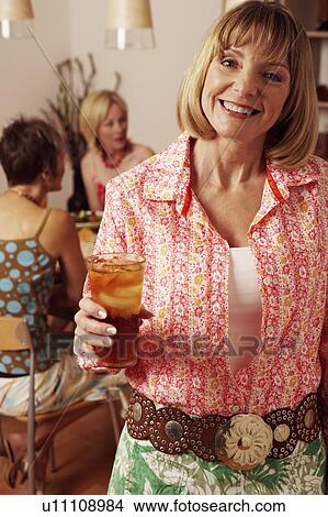 Picture - Portrait of a mature woman holding a glass with her friends sitting behind her. Fotosearch