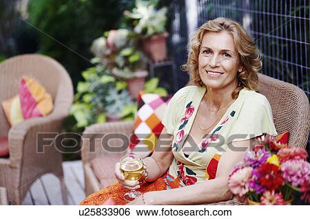 Stock Photograph - Portrait of a mature woman holding a glass of wine and smiling. Fotosearch