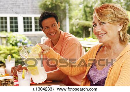 Stock Photo - Portrait of a mature woman pouring lemon juice in a glass with a mature man sitting beside her. Fotosearch