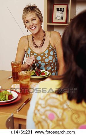 Stock Image - Portrait of a mature woman sitting at the dining table with her friend. Fotosearch